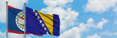 Belize ve Bosna Hersek bayrağı birlikte beyaz bulutlu mavi gökyüzüne karşı rüzgarda sallayarak. Diplomasi kavramı, uluslararası ilişkiler.