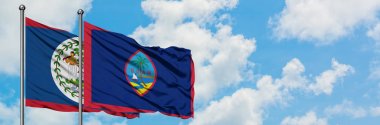 Belize ve Guam bayrağı birlikte beyaz bulutlu mavi gökyüzüne karşı rüzgarda sallayarak. Diplomasi kavramı, uluslararası ilişkiler.