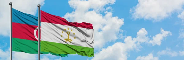 Azerbaidzanin ja Tadzikistanin lippu heiluttaa tuulessa valkoista pilvistä sinistä taivasta vasten yhdessä. Diplomatian käsite, kansainväliset suhteet . — kuvapankkivalokuva