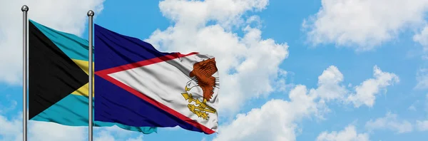 一緒に白い曇り青い空に対して風に手を振るバハマとアメリカのサモアの旗。外交概念、国際関係. — ストック写真