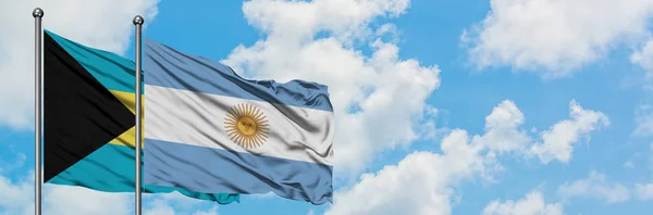 Bandera de Bahamas y Argentina ondeando en el viento contra el cielo azul nublado blanco juntos. Concepto diplomático, relaciones internacionales . — Foto de Stock