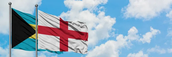 Bandera de Bahamas e Inglaterra ondeando en el viento contra el cielo azul nublado blanco juntos. Concepto diplomático, relaciones internacionales . — Foto de Stock