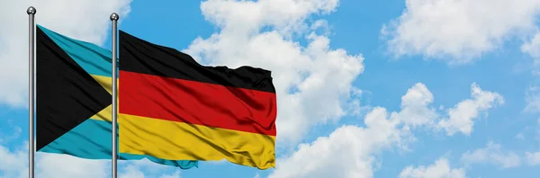 Bahamas e la Germania bandiera sventolando nel vento contro bianco cielo blu nuvoloso insieme. Concetto di diplomazia, relazioni internazionali . — Foto Stock