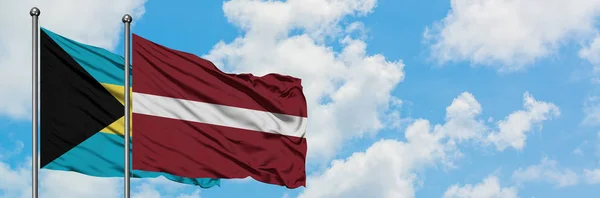Bahamy i Łotwa flaga machając w wiatr przed białym zachmurzone błękitne niebo razem. Koncepcja dyplomacji, stosunki międzynarodowe. — Zdjęcie stockowe