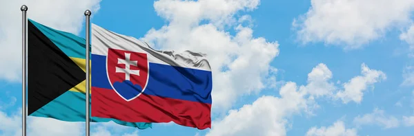 Bahamy i Słowacji flagi machając w wiatr przed białym zachmurzone błękitne niebo razem. Koncepcja dyplomacji, stosunki międzynarodowe. — Zdjęcie stockowe