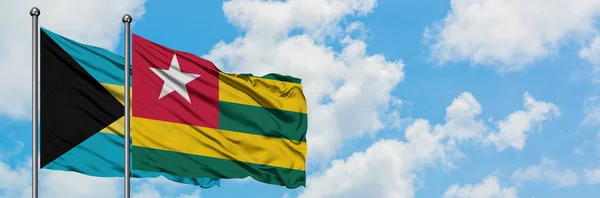 Bandera de Bahamas y Togo ondeando en el viento contra el cielo azul nublado blanco juntos. Concepto diplomático, relaciones internacionales . —  Fotos de Stock