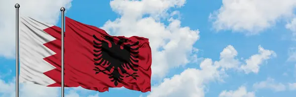 Bahrain and Albania flag waving in the wind against white cloudy blue sky together. Diplomacy concept, international relations. — Stock Photo, Image