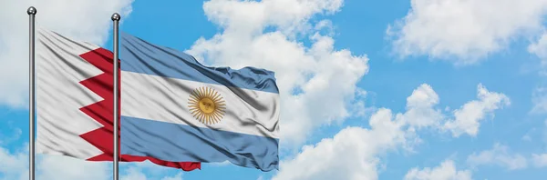 Bandera de Bahréin y Argentina ondeando en el viento contra el cielo azul nublado blanco juntos. Concepto diplomático, relaciones internacionales . — Foto de Stock