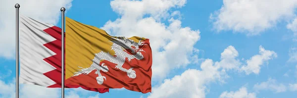 Bandera de Bahréin y Bután ondeando en el viento contra el cielo azul nublado blanco juntos. Concepto diplomático, relaciones internacionales . — Foto de Stock