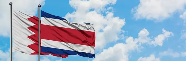 Bandeira do Bahrein e da Costa Rica agitando no vento contra o céu azul nublado branco juntos. Conceito de diplomacia, relações internacionais . — Fotografia de Stock