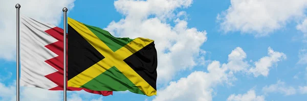 Bandera de Bahréin y Jamaica ondeando en el viento contra el cielo azul nublado blanco juntos. Concepto diplomático, relaciones internacionales . — Foto de Stock