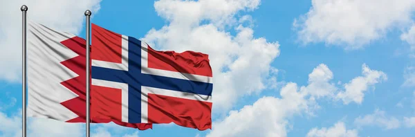 Bandera de Bahréin y Noruega ondeando en el viento contra el cielo azul nublado blanco juntos. Concepto diplomático, relaciones internacionales . — Foto de Stock