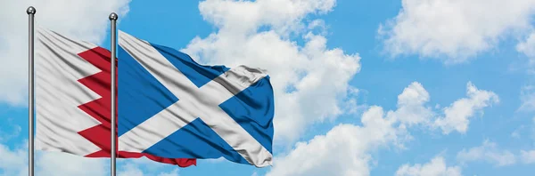 Bahrein e a bandeira da Escócia agitando no vento contra o céu azul nublado branco juntos. Conceito de diplomacia, relações internacionais . — Fotografia de Stock