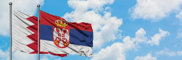 Bandera de Bahréin y Serbia ondeando en el viento contra el cielo azul nublado blanco juntos. Concepto diplomático, relaciones internacionales . — Foto de Stock