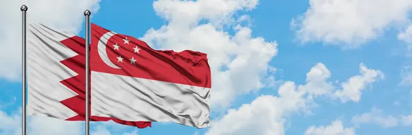 Bahrein e bandeira de Singapura agitando no vento contra o céu azul nublado branco juntos. Conceito de diplomacia, relações internacionais . — Fotografia de Stock