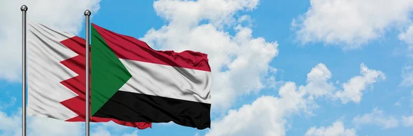 Bandera de Bahréin y Sudán ondeando en el viento contra el cielo azul nublado blanco juntos. Concepto diplomático, relaciones internacionales . — Foto de Stock