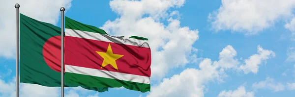 Bandera de Bangladesh y Surinam ondeando en el viento contra el cielo azul nublado blanco juntos. Concepto diplomático, relaciones internacionales . — Foto de Stock