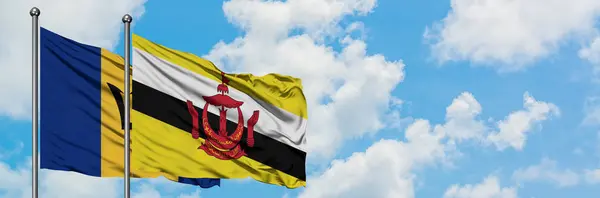 Bandera de Barbados y Brunei ondeando en el viento contra el cielo azul nublado blanco juntos. Concepto diplomático, relaciones internacionales . —  Fotos de Stock