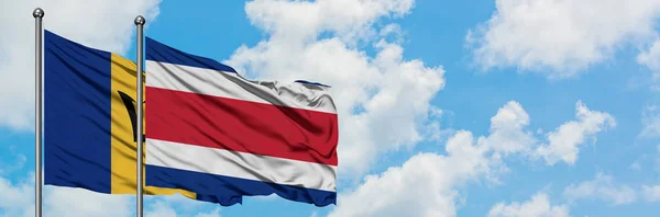 Barbados e la bandiera del Costa Rica sventolano insieme nel vento contro il cielo blu nuvoloso bianco. Concetto di diplomazia, relazioni internazionali . — Foto Stock