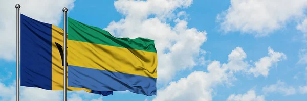 Barbados i Gabon flaga machając w wiatr przed białym zachmurzone błękitne niebo razem. Koncepcja dyplomacji, stosunki międzynarodowe. — Zdjęcie stockowe