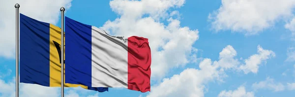 Barbados e la Francia bandiera sventolando nel vento contro bianco cielo blu nuvoloso insieme. Concetto di diplomazia, relazioni internazionali . — Foto Stock