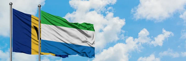 Barbados und Sierra Leone schwenken gemeinsam die Flagge im Wind vor dem wolkenverhangenen blauen Himmel. Diplomatie-Konzept, internationale Beziehungen. — Stockfoto