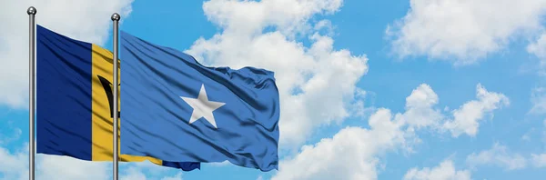 Bandera de Barbados y Somalia ondeando en el viento contra el cielo azul nublado blanco juntos. Concepto diplomático, relaciones internacionales . — Foto de Stock