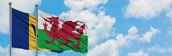 Barbados e a bandeira do País de Gales agitando no vento contra o céu azul nublado branco juntos. Conceito de diplomacia, relações internacionais . — Fotografia de Stock