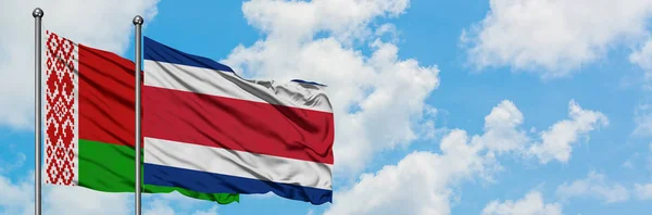 Bandera de Bielorrusia y Costa Rica ondeando en el viento contra el cielo azul nublado blanco juntos. Concepto diplomático, relaciones internacionales . — Foto de Stock