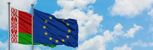 La Bielorussia e la bandiera dell'Unione europea sventolano insieme nel vento contro il bianco cielo blu nuvoloso. Concetto di diplomazia, relazioni internazionali . — Foto Stock