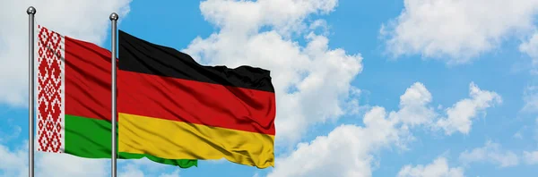 Bielorrússia e Alemanha bandeira acenando no vento contra o céu azul nublado branco juntos. Conceito de diplomacia, relações internacionais . — Fotografia de Stock