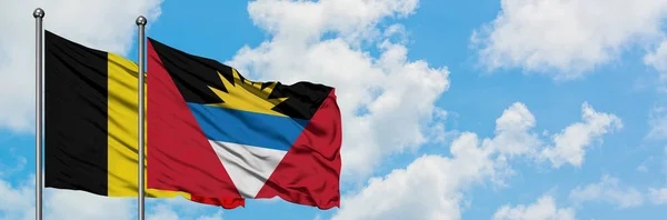 Belgien och Antigua och Barbuda flagga vifta i vinden mot vit grumlig blå himmel tillsammans. Diplomatisk koncept, internationella relationer. — Stockfoto