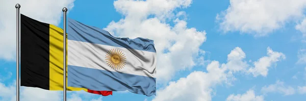 Bandera de Bélgica y Argentina ondeando en el viento contra el cielo azul nublado blanco juntos. Concepto diplomático, relaciones internacionales . — Foto de Stock