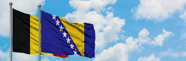 Bandera de Bélgica y Bosnia Herzegovina ondeando en el viento contra el cielo azul nublado blanco juntos. Concepto diplomático, relaciones internacionales . — Foto de Stock