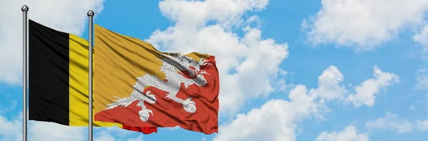 België en Bhutan vlag zwaaien in de wind tegen witte bewolkte blauwe hemel samen. Diplomatie concept, internationale betrekkingen. — Stockfoto