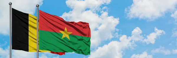 Bandera de Bélgica y Burkina Faso ondeando en el viento contra el cielo azul nublado blanco juntos. Concepto diplomático, relaciones internacionales . — Foto de Stock
