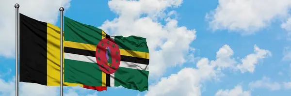 Bandera de Bélgica y Dominica ondeando en el viento contra el cielo azul nublado blanco juntos. Concepto diplomático, relaciones internacionales . — Foto de Stock
