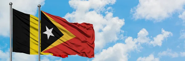 Bandera de Bélgica y Timor Oriental ondeando en el viento contra el cielo azul nublado blanco juntos. Concepto diplomático, relaciones internacionales . —  Fotos de Stock