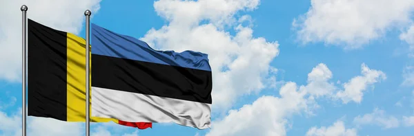 België en Estland vlag zwaaien in de wind tegen witte bewolkte blauwe hemel samen. Diplomatie concept, internationale betrekkingen. — Stockfoto