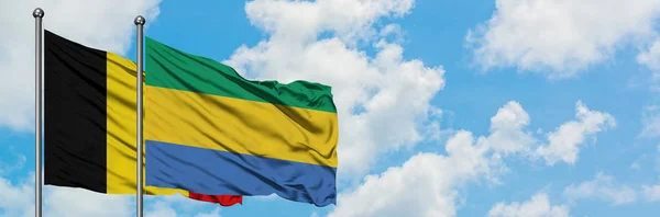 Bandera de Bélgica y Gabón ondeando en el viento contra el cielo azul nublado blanco juntos. Concepto diplomático, relaciones internacionales . — Foto de Stock