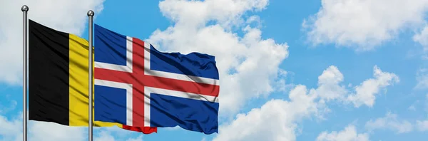 Bandera de Bélgica e Islandia ondeando en el viento contra el cielo azul nublado blanco juntos. Concepto diplomático, relaciones internacionales . — Foto de Stock