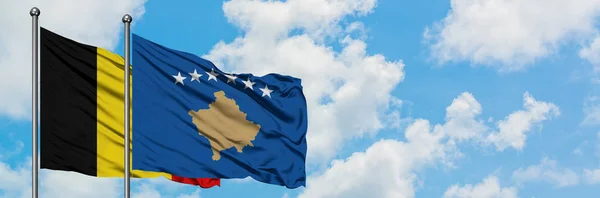 Gemeinsam wehen belgische und kosovarische Flaggen im Wind vor dem wolkenverhangenen blauen Himmel. Diplomatie-Konzept, internationale Beziehungen. — Stockfoto