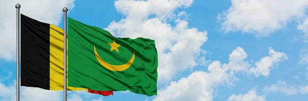 Bandera de Bélgica y Mauritania ondeando en el viento contra el cielo azul nublado blanco juntos. Concepto diplomático, relaciones internacionales . — Foto de Stock