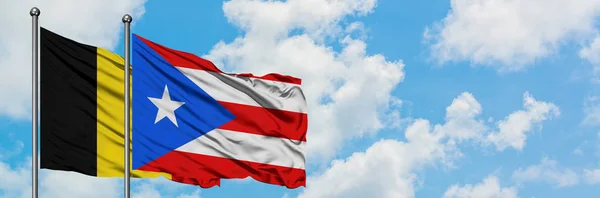Bandera de Bélgica y Puerto Rico ondeando en el viento contra el cielo azul nublado blanco juntos. Concepto diplomático, relaciones internacionales . — Foto de Stock
