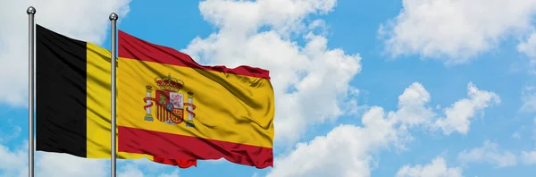 Belgien und Spanien wehen gemeinsam im Wind vor dem wolkenverhangenen blauen Himmel. Diplomatie-Konzept, internationale Beziehungen. — Stockfoto