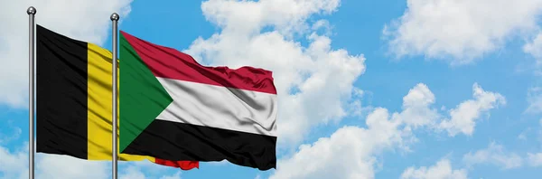 Bandera de Bélgica y Sudán ondeando en el viento contra el cielo azul nublado blanco juntos. Concepto diplomático, relaciones internacionales . — Foto de Stock