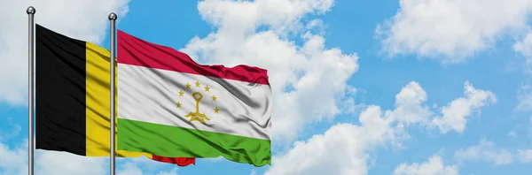 Bandera de Bélgica y Tayikistán ondeando en el viento contra el cielo azul nublado blanco juntos. Concepto diplomático, relaciones internacionales . — Foto de Stock