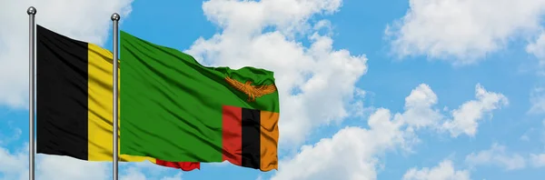 Bandera de Bélgica y Zambia ondeando en el viento contra el cielo azul nublado blanco juntos. Concepto diplomático, relaciones internacionales . — Foto de Stock