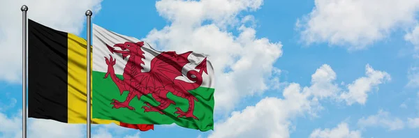 A bandeira da Bélgica e do País de Gales agitando no vento contra o céu azul nublado branco juntos. Conceito de diplomacia, relações internacionais . — Fotografia de Stock