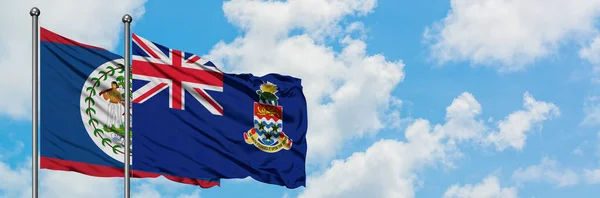 Bandera de Belice y las Islas Caimán ondeando en el viento contra el cielo azul nublado blanco juntos. Concepto diplomático, relaciones internacionales . — Foto de Stock